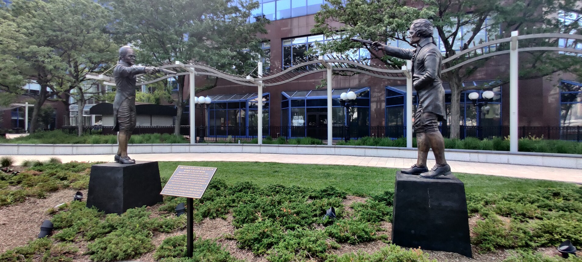 Statue of Alexander Hamilton pointing a pistol at a statue of Aaron Burr, who is doing the same. A plaque in the middle explains this is where the famous duel between the two took place, and Hamilton died.