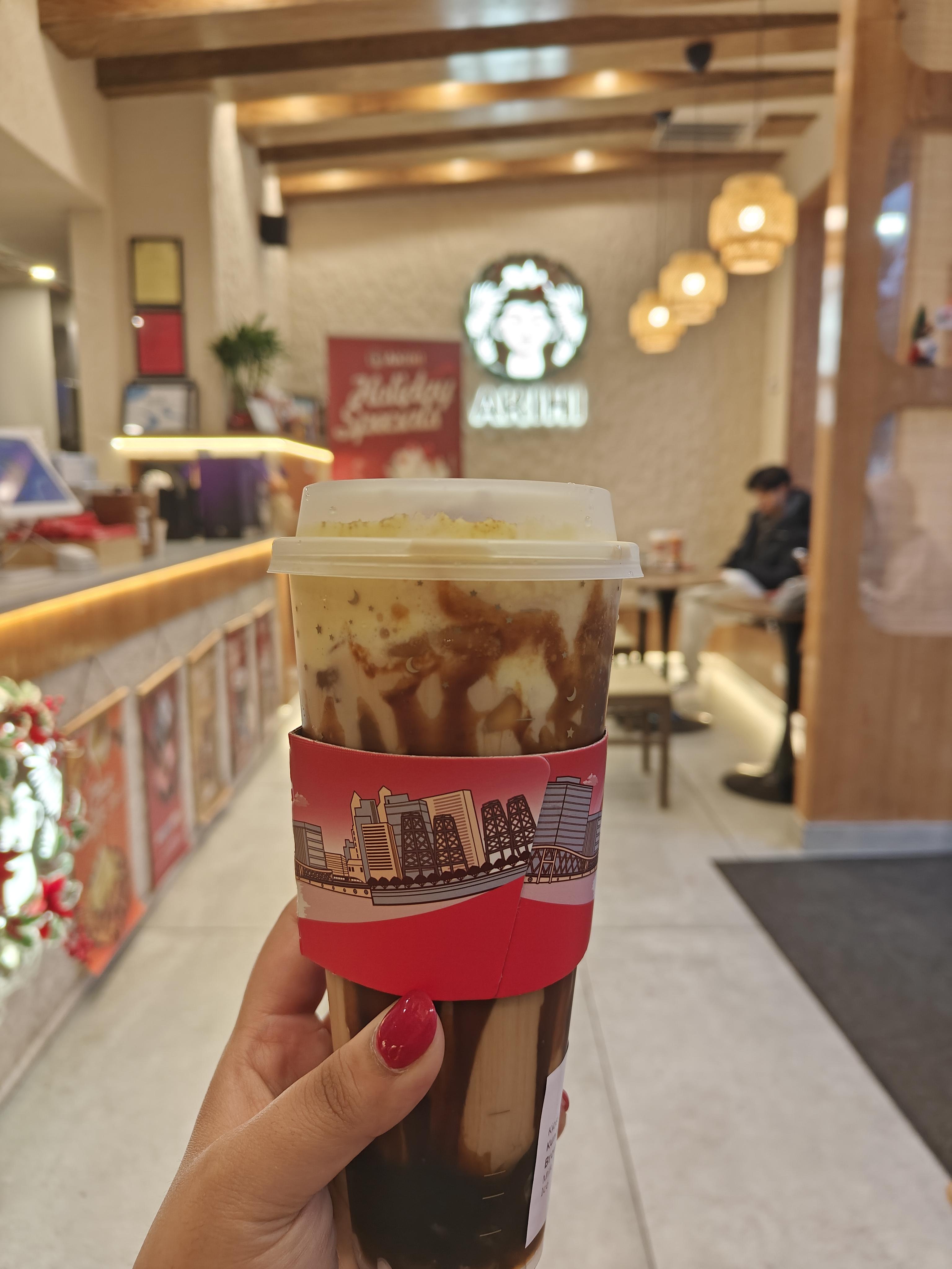 A hand with painted red nails holding up a cup of boba with the store blurred in the background