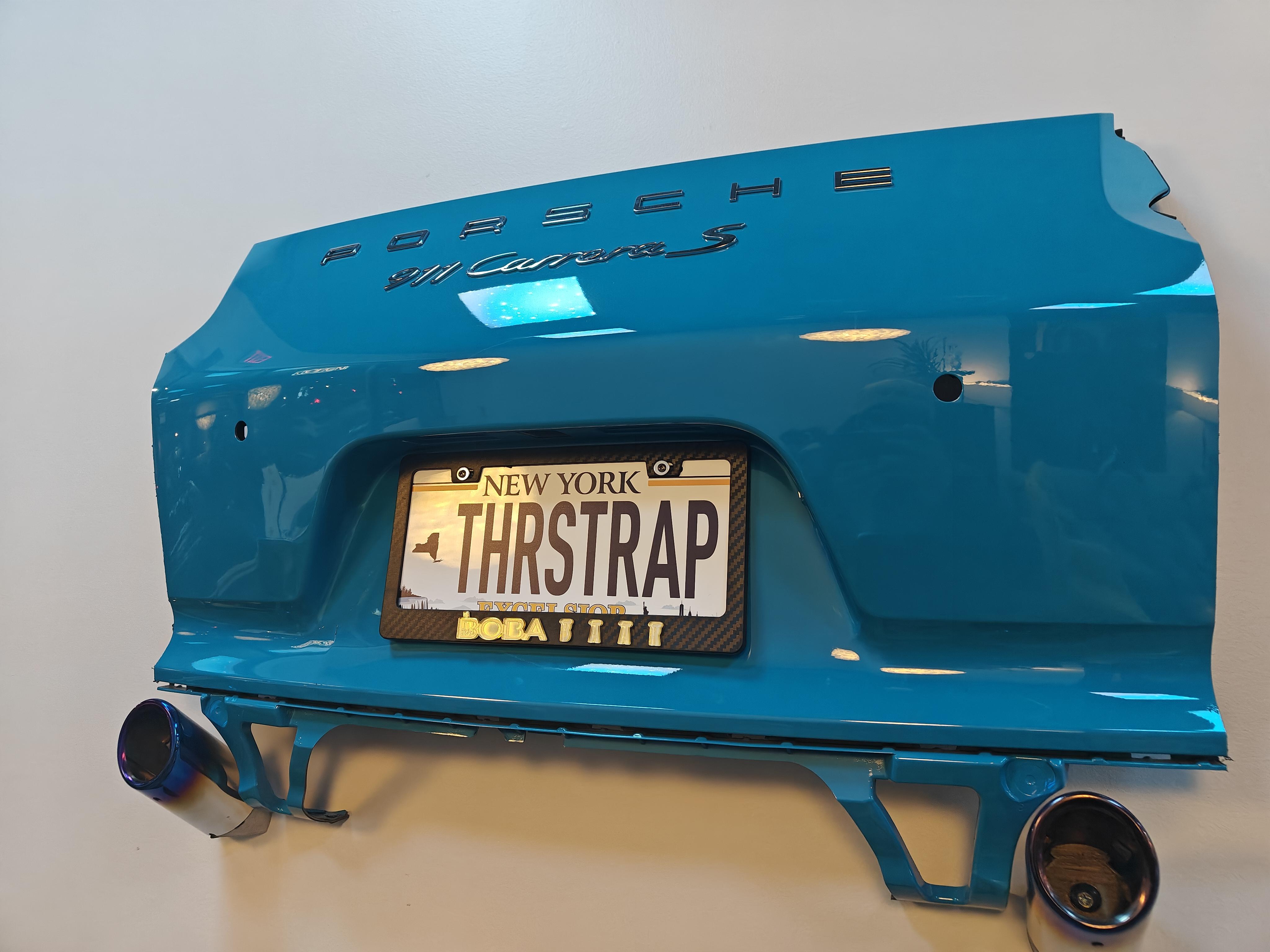 A car bumper mounted to the wall with a fake New York license plate that says THRSTRAP.