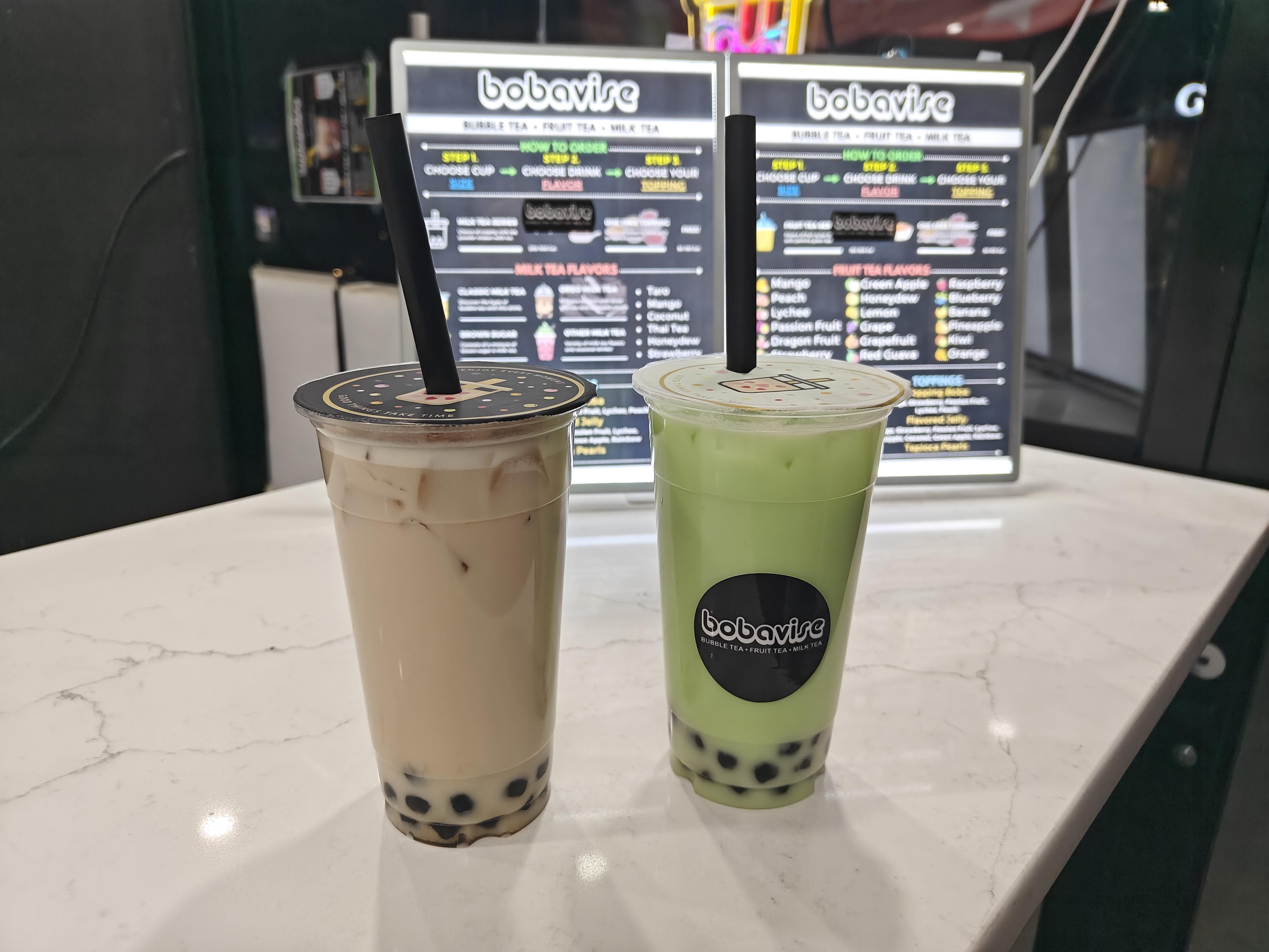 Two boba drinks, with a blurred out menu in the background.