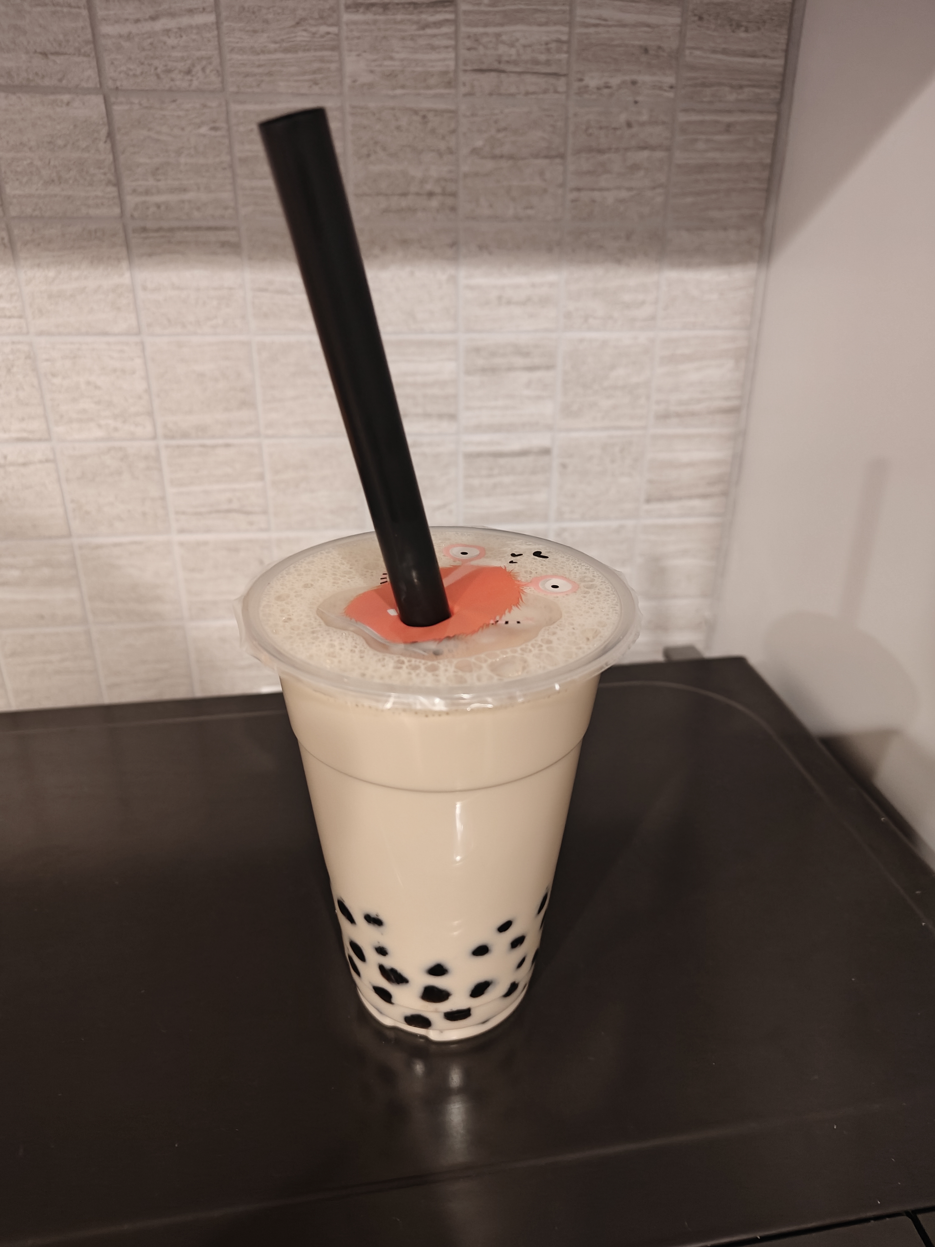 Boba tea in a clear plastic cup with a black plastic straw sitting on top of a black microwave