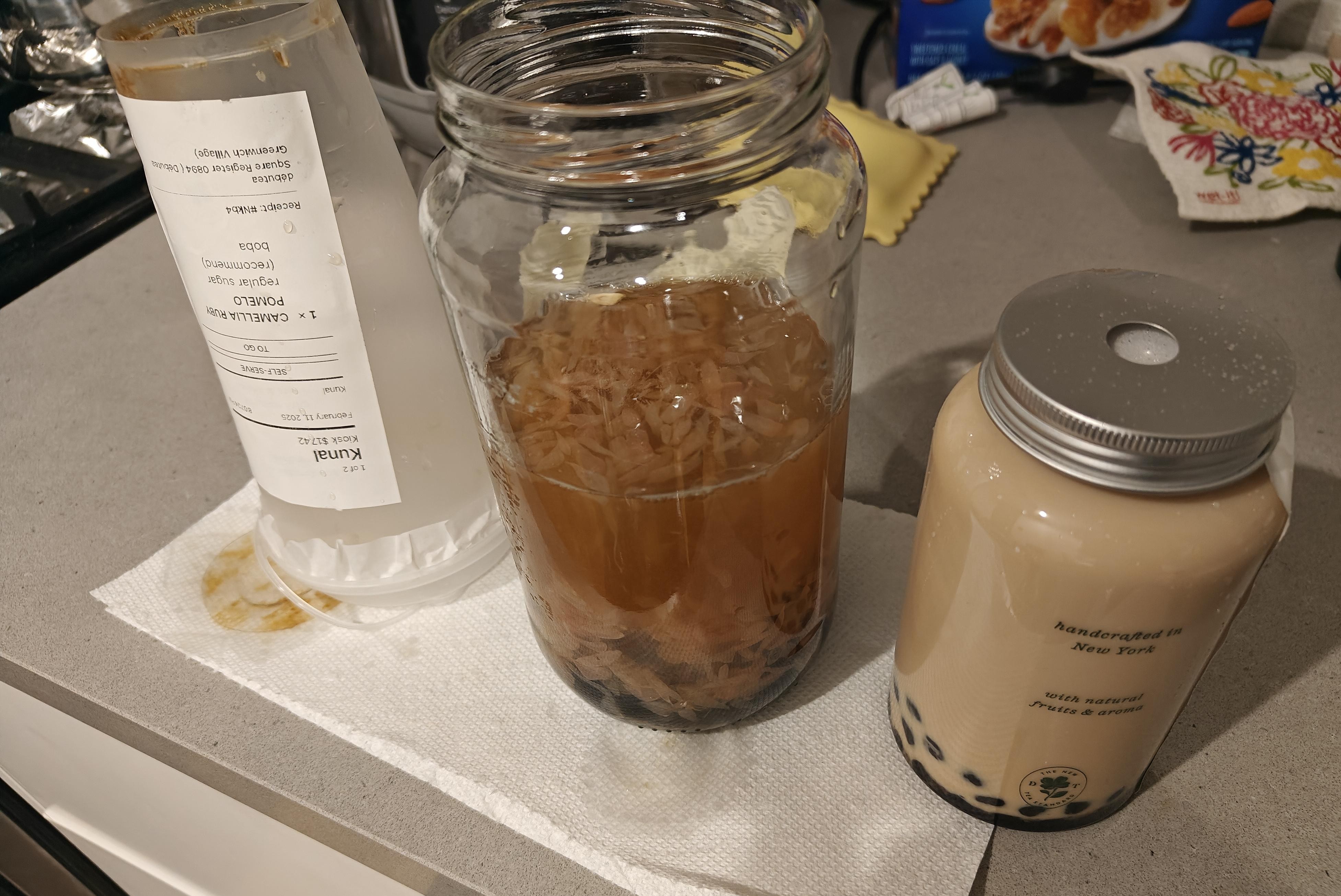 From left to right, an upside down empty plastic boba tea cup, a mason jar with the camellia ruby pomelo tea and then a cute plastic mason jar that's half the size of the previous one with BOBO milk tea.