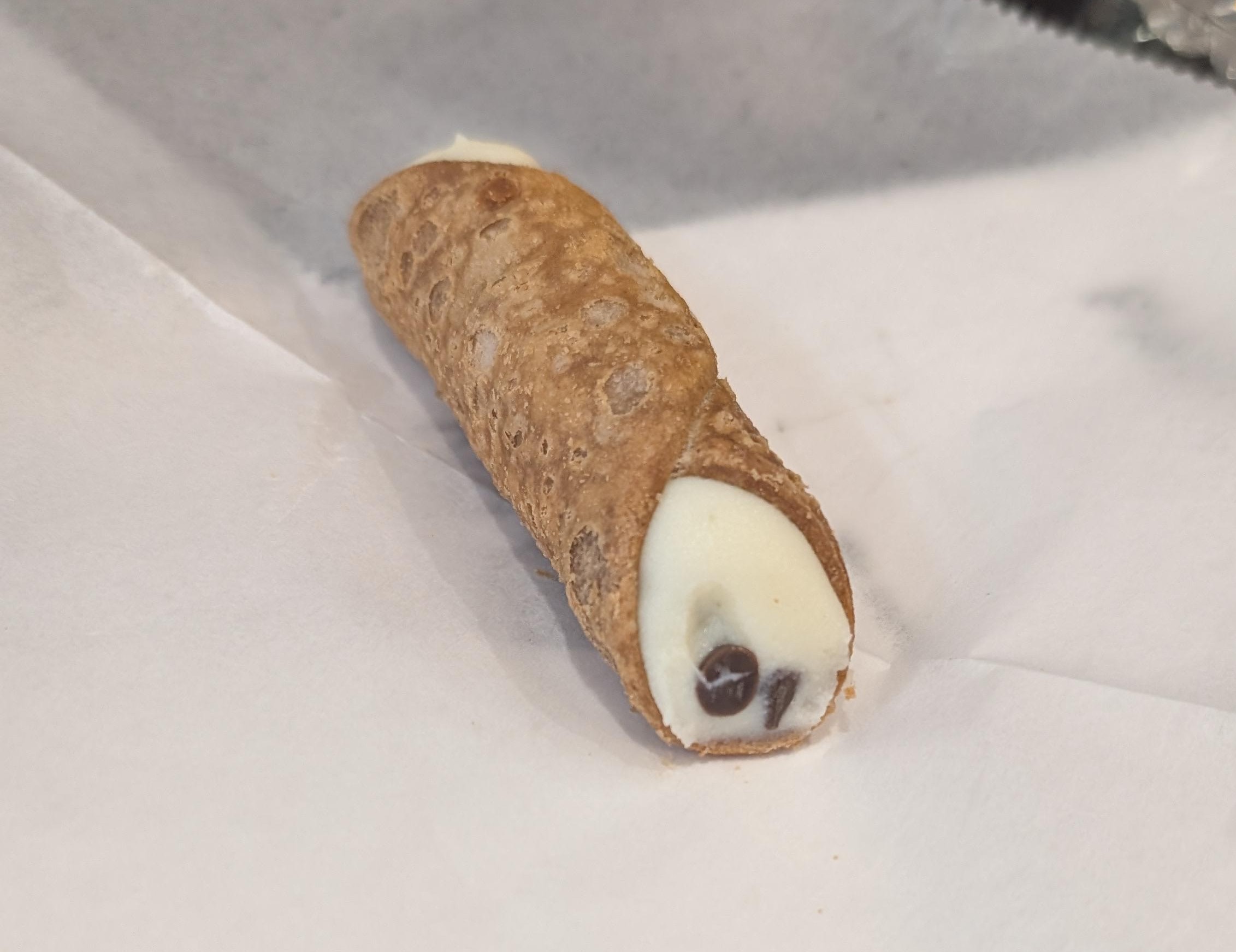 A single cannoli with a few chocolate chips on the end sitting on wax paper